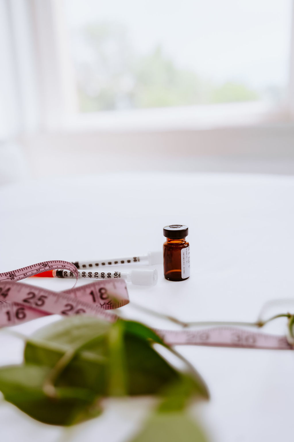 Amber medication vial, syringe, and pink measuring tape arranged on a white surface